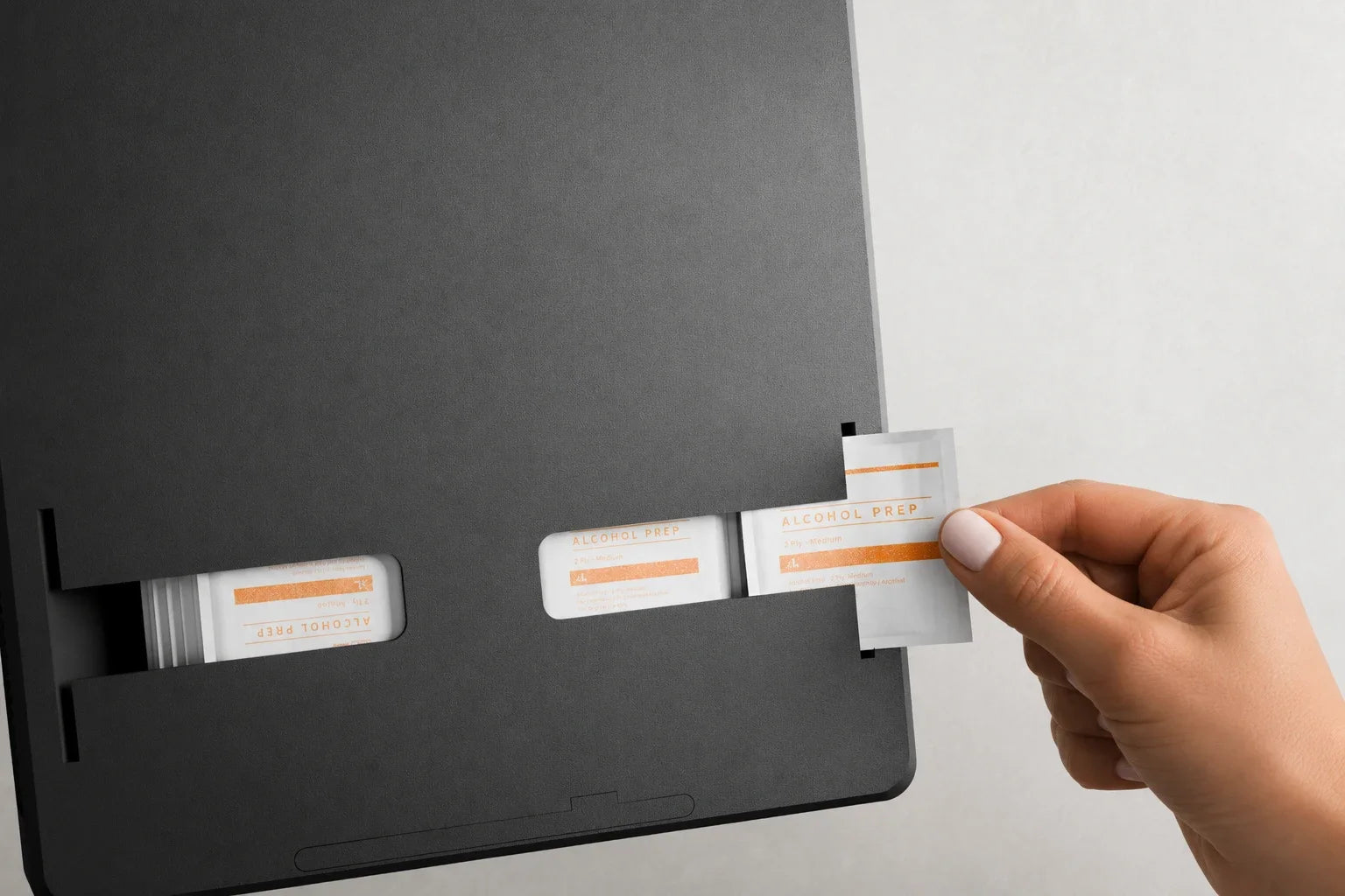 A hand pulling a wrapped prep pad from the Routine Box dispenser